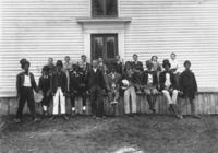 Portrait of actors in blackface and band members in front of a clabbered building in East Dover, Vt.